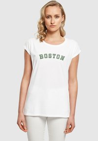 Weißes Baumwoll-T-Shirt mit umgeschlagenen kurzen Ärmeln, auf dem die grüne Aufschrift "BOSTON" über die Brust gedruckt ist. Einfaches, unauffälliges Design.
