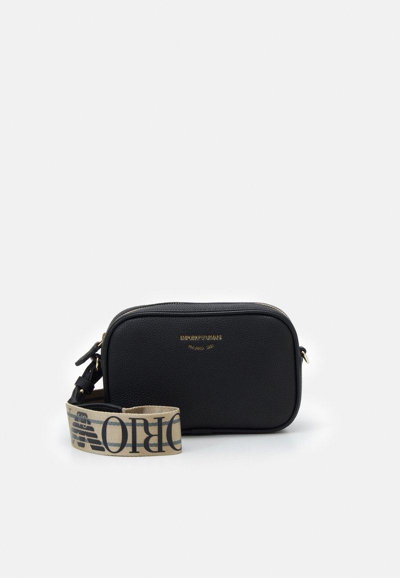 Sac en cuir noir à bandoulière, doté d'une fermeture éclair, présentant un motif texturé et une sangle beige avec des lettres noires. Détail du logo doré visible.