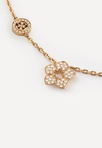 Bracciale in oro con un charm a forma di fiore decorato con cristalli trasparenti, accompagnato da un charm circolare con un logo, entrambi con dettagli intricati.