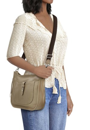 Beige leather shoulder bag with a front pocket, brown adjustable strap, and smooth texture. Model is wearing a cream sweater and blue jeans.