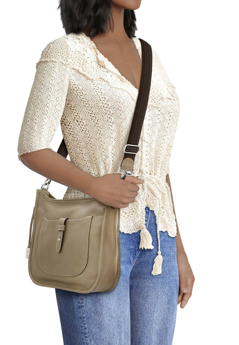 Beige Leder-Schultertasche mit einer Fronttasche, braunem verstellbarem Trageriemen und glatter Textur. Das Model trägt einen cremfarbenen Pullover und blaue Jeans.