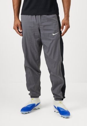 Nike track pants in gray and black, featuring a loose fit, lightweight fabric, elastic cuffs, and a white swoosh logo on the front.