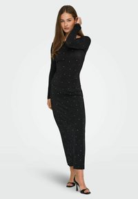Vestido negro de manga larga con una silueta ajustada, adornado con pequeños puntos plateados. Textura suave, hasta la rodilla, combinado con tacones negros.