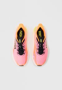 Chaussures de sport rose vif avec une tige en maille texturée, des accents orange, des lacets noirs et une semelle rembourrée dotée d'un détail translucide.