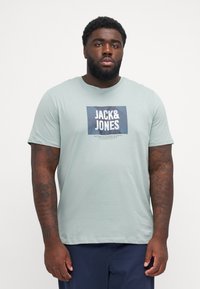 Απαλή πράσινη βαμβακερή μπλούζα με κοντό μανίκι, με τετράγωνο ναυτικό λογότυπο "JACK&JONES" στο κέντρο του στήθους. Μικρή λαιμόκοψη.