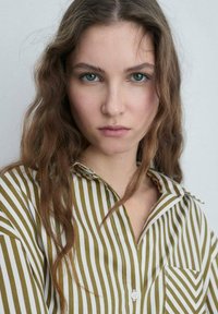 Camicia a righe con linee verticali verdi e bianche, in tessuto morbido, colletto con bottoni e taschino sul petto.