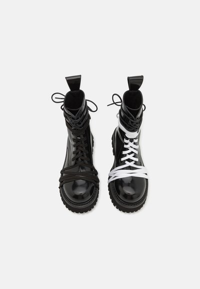 Botines en blanco y negro con acabado de charol brillante, que presentan cordones en contraste, puntera redondeada y suela de goma gruesa.
