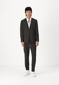 Costum gri cu carouri, cu o croială ajustată, sacou cu un rând de nasturi și pantaloni asortați. Purtați peste o cămașă albă, asociați cu adidași albi.