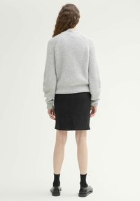 Grauer, gerippter Pullover mit Rundhalsausschnitt, kombiniert mit einem schwarzen Jeansrock, der über dem Knie endet. Schwarz Schuhe und Socken runden das Outfit ab.