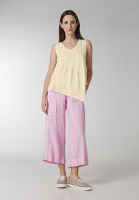 Top galben fără mâneci, cu decolteu în V și design peplum, asociat cu culottes din in roz deschis, cu buzunare aplicate și o croială lejeră.
