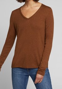 Brązowy sweter z długim rękawem i dekoltem w kształcie litery V, wykonany z miękkiej dzianiny. Posiada dopasowane rękawy i luźny krój, idealnie komponujący się z niebieskimi dżinsami.