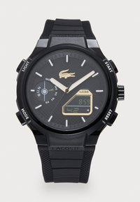 Digital watch with a black silicone strap and textured black dial. Features gold accents, white hour markers, and digital display for time.