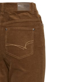 Brown corduroy jeans with a textured fabric, featuring back pockets and contrasting beige stitching. Brand label visible at the waist.