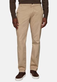 Beige cotton chinos with a straight-leg cut, featuring a front button closure, side pockets, and a smooth texture, paired with dark brown sneakers.