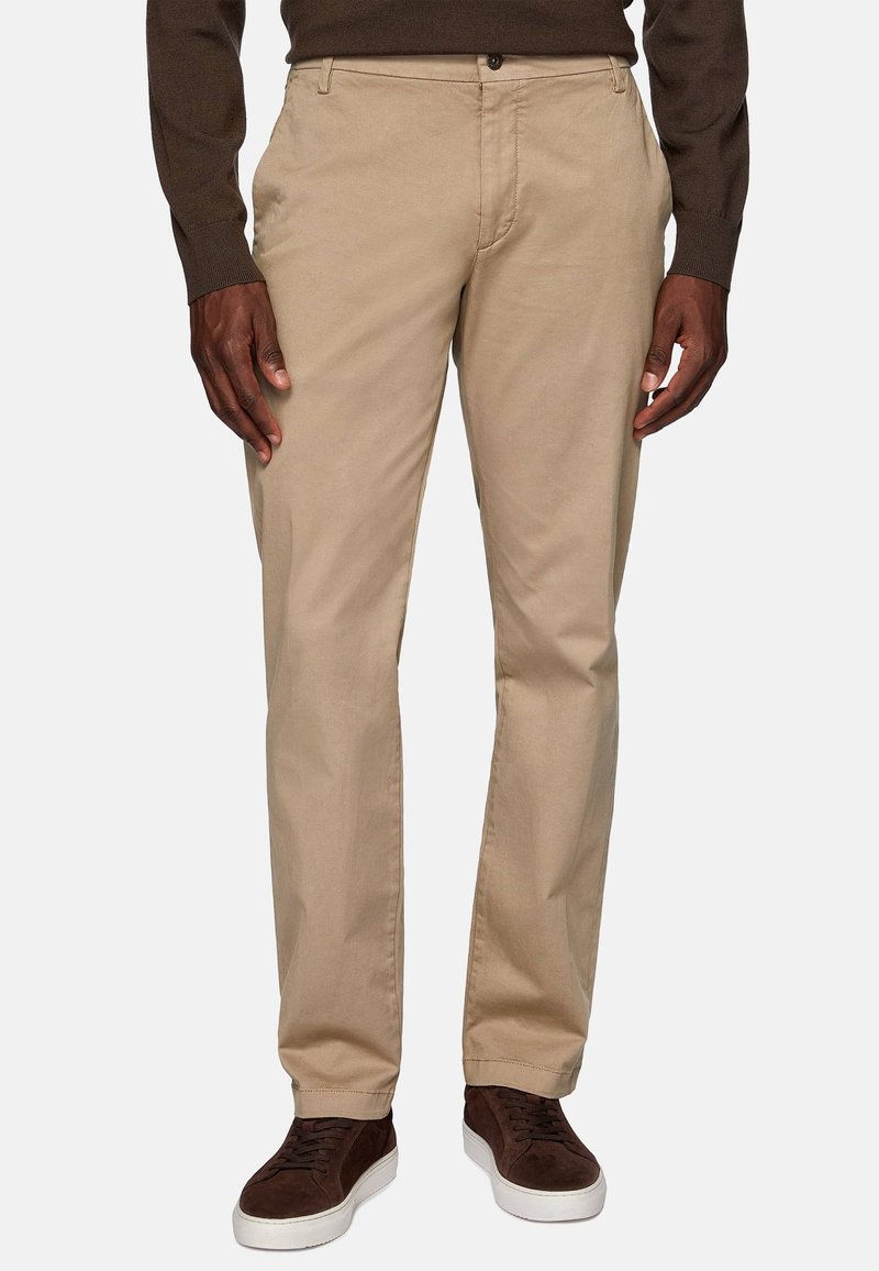 Beige cotton chinos with a straight-leg cut, featuring a front button closure, side pockets, and a smooth texture, paired with dark brown sneakers.