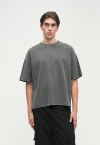 Γκρι υπερμεγέθη t-shirt με κοντά μανίκια, στρογγυλή λαιμόκοψη και ένα μικρό λογότυπο τυπωμένο στην αριστερή πλευρά. Φορεμένο με μαύρες cargo βερμούδες.