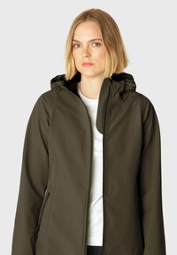 Chaqueta softshell verde oscuro con capucha, frente con cremallera y bolsillos laterales. Textura suave con material flexible para comodidad y movilidad.