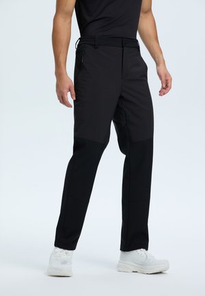 Pantalones de exterior negros hechos de un tejido resistente al agua, con una textura suave, bolsillos con cremallera y paneles de rodilla reforzados.