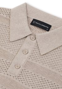 Jasno beżowa koszulka polo wykonana z dzianiny, z teksturowanym wzorem, trzema guzikami i klasycznym kołnierzykiem. Widoczna metka marki.