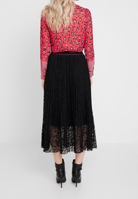 Rød leopardprint langærmet bluse med stribede manchetter, parret med en plisseret sort blonde-nederdel. Sorte ankelstøvler fuldender sættet.