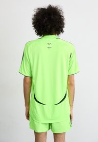 Neon žalia sportinė maikutė ir šortai, su trumpomis rankovėmis, juodais akcentais ir logotipo detale nugaroje. Lygus, lengvas audinys.