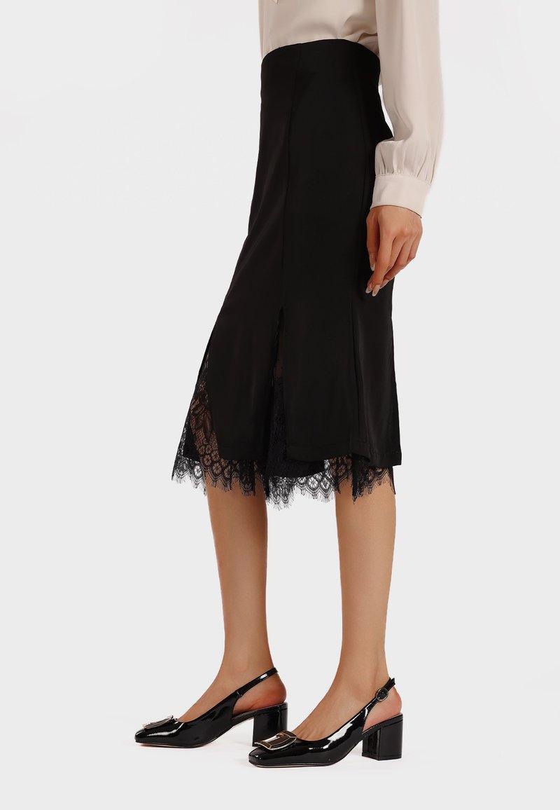 Falda negra con un dobladillo de encaje, que presenta una longitud hasta la mitad de la pantorrilla, aberturas laterales y una textura suave. Combinada con tacones slingback negros de charol.