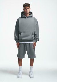 Grå overdimensjonert hettegenser med en frontlomme og matchende grå shorts. Laget av mykt materiale, har snor i livet og ribbede mansjetter.