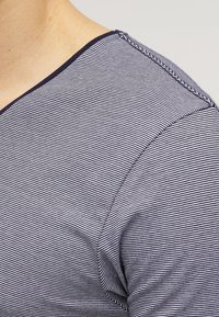 Stribet t-shirt med marineblå og hvide lodrette striber, v-halsdesign og blød stofstruktur med synlige sømme langs kraven.