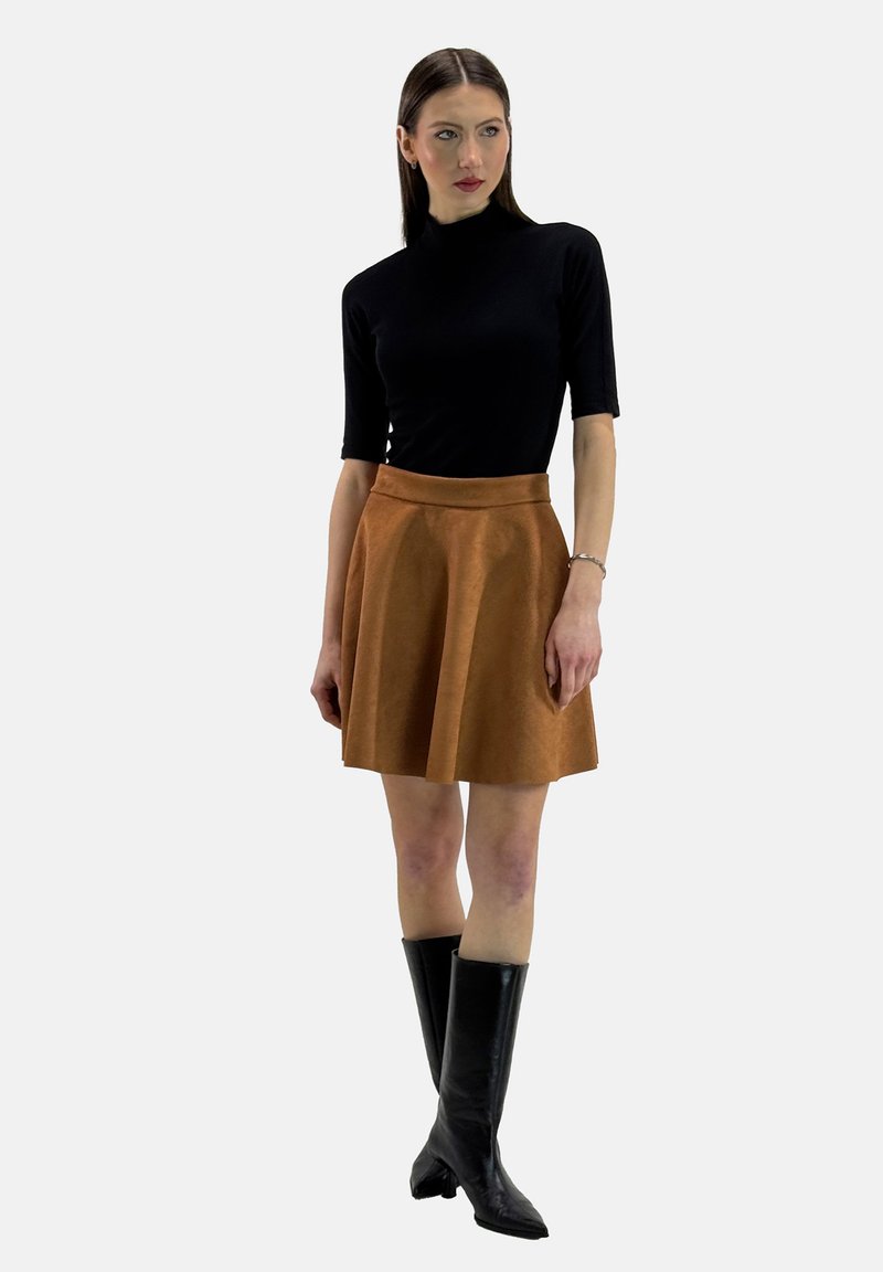 Jersey negro de manga corta con cuello alto combinado con una falda marrón de corte A. La modelo lleva botas negras hasta la rodilla, mostrando texturas suaves y líneas limpias.