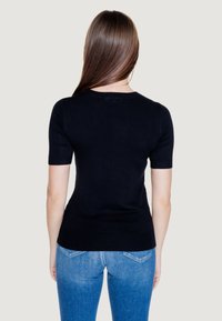 Top in maglia nera a maniche corte con scollatura tonda e orlo a coste. Indossato con jeans in denim blu, che mostrano un design aderente e una texture liscia.