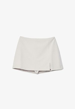 Bež visokerožni skort z majhnim sprednjim razrezom na desni strani, ki združuje videz krila s kratkimi hlačami spodaj.