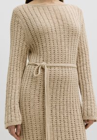 Beiges Strickkleid mit lockerer Passform, das ein strukturiertes Muster, lange Ärmel und einen Stoffgürtel, der an der Taille gebunden ist, aufweist.