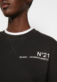 Sudadera negra con el texto blanco "N°21 MILANO - VIA SANTO SPIRITO," con cuello redondo y detalle de costura visible.