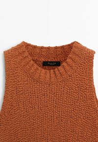 Pull en tricot couleur rouille avec un col rond et un tissu épais et texturé. Étiquette visible à l'intérieur du col. Sans manches.
