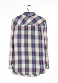 Chemise à manches longues à carreaux beige, bleu et bordeaux avec un ourlet effiloché, des poignets à boutons et un col pointu. Suspendue à un crochet noir.