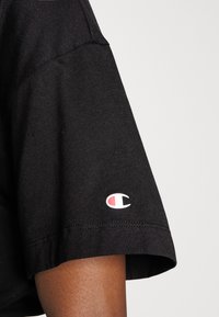 Černé krátké rukávy tričko vyrobené z bavlny s hladkou texturou. Na levém rukávu se nachází malé bílé a červené logo "Champion".