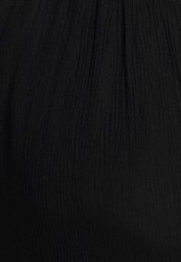 Tissu noir texturé avec un design froissé, présentant une finition douce et plissée. Le matériau semble léger et tombe doucement.
