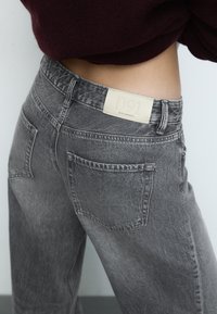 Sive traperice s teksturiranim završetkom, s dva stražnja džepa i krem oznakom označenom "D91" na struku.