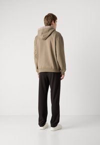 Sudadera marrón con un forro ligero y capucha, combinada con pantalones negros. Los materiales parecen suaves y casuales, diseñados para la comodidad.