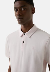 Lys rosa polo t-shirt med krave, knaplukning med to sorte knapper og et lille præget logo på brystet.