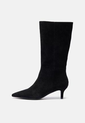 Bota de tornozelo em camurça preta com bico fino, salto delgado e textura suave, apresentando uma silhueta ajustada e sem hardware visível.