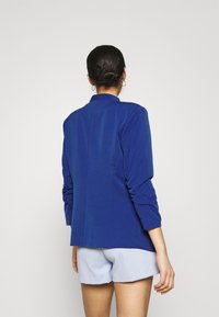 Blå blazer med långa ärmar och krage. Har en rak skärning och textil med struktur, skräddarsydd passform och minimalistisk design.