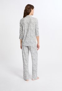 Zestaw odzieży domowej w panterkę z lekkiego materiału. Bluzka z długim rękawem i spodnie długości pełnej z szaro-czarnym wzorem na białym tle.