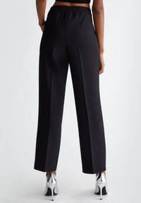 Pantaloni neri a gamba larga realizzati in tessuto morbido con una vita elasticizzata. Presentano un design semplice con una silhouette elegante e senza tasche visibili.