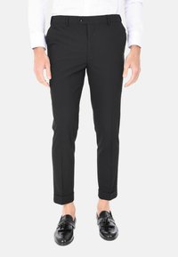Pantaloni neri su misura con vestibilità slim, caratterizzati da una parte anteriore piatta, orli con risvolto e tasche laterali, abbinati a mocassini in pelle nera.