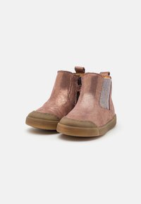 Botas de tornozelo metálicas cor-de-rosa com painéis laterais elásticos e uma alça na parte traseira. Apresentam uma sola em borracha e um material superior liso e texturizado.