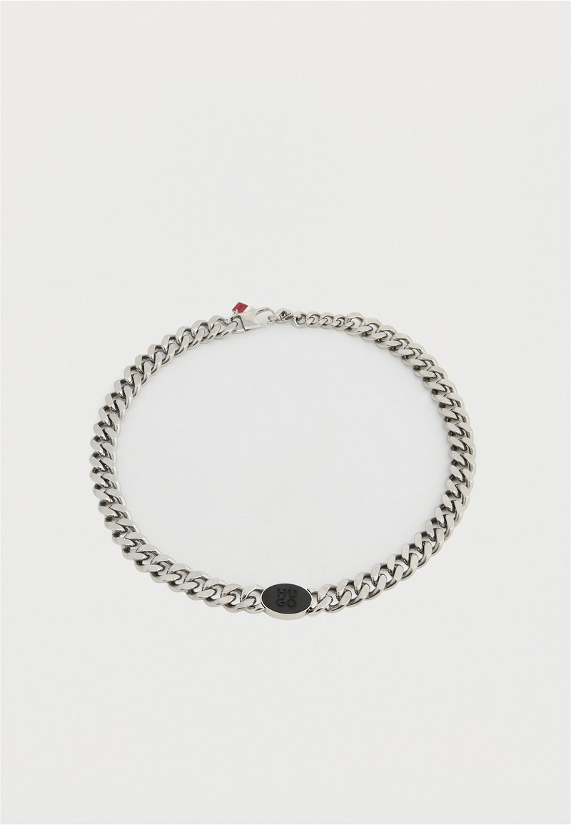 Collana choker a catena in metallo argentato con grandi maglie, caratterizzata da un logo ovale nero e un piccolo dettaglio rosso alla chiusura. Texture liscia.