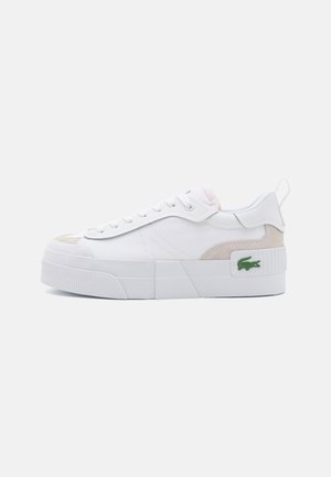 Biały niski sneaker z grubą podeszwą, sznurowany, beżowe zamszowe detale i zielone logo krokodyla przy pięcie na jednolitym tle.