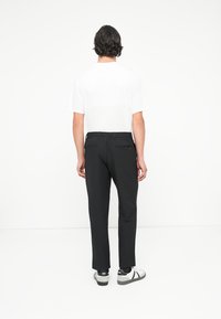 Pantaloni negri cu o croială relaxată, talie elastică, două buzunare pe spate, asociați cu o cămașă albă cu mânecă scurtă și încălțăminte casual.