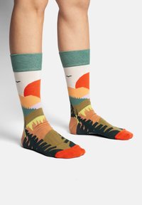 Baumwollsocken mit einem Landschaftsdesign von Bergen und einem Sonnenuntergang, hauptsächlich in Orange-, Grün- und Erdtönen; gerippter Knöchelabschluss.